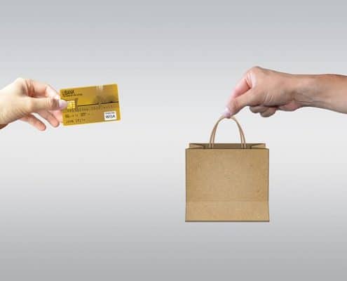 Graphic showing two desktops facing each other - one with a hand reaching out of it holding a bag, the other with a hand reaching out of it holding a credit card.