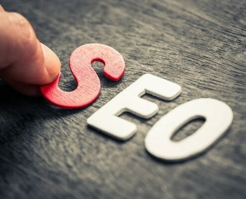 A hand placing the red letter S on a table to spell out SEO
