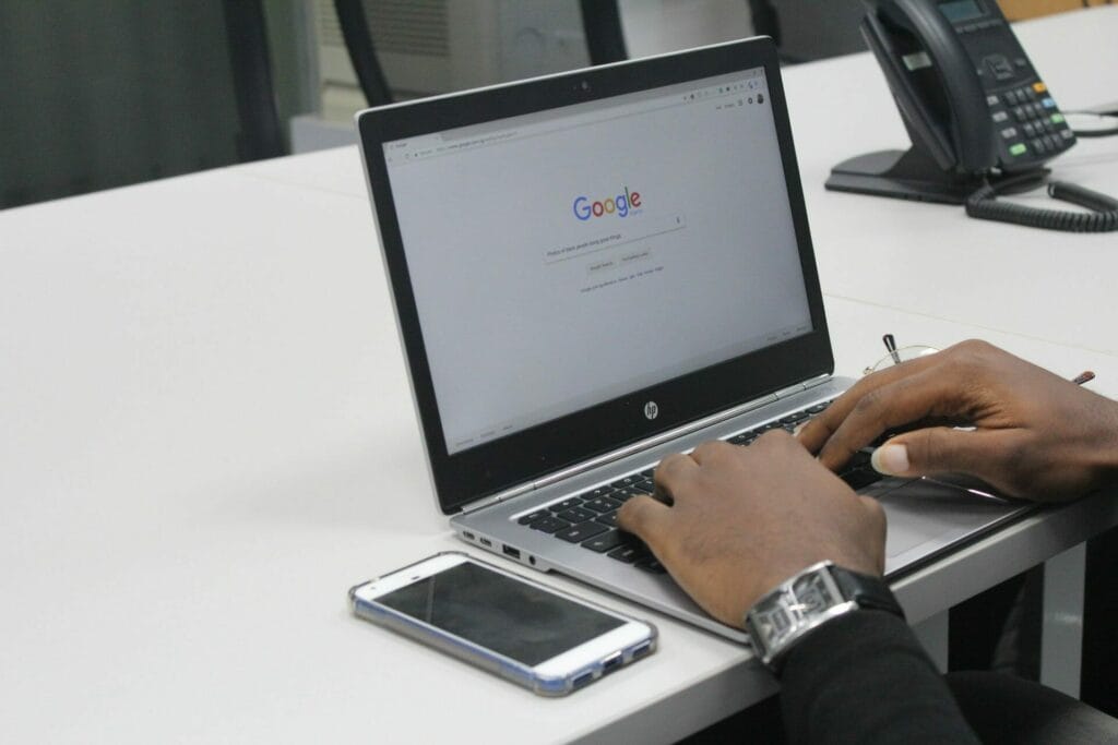 A man with a smartphone typing on a laptop in Google Search.