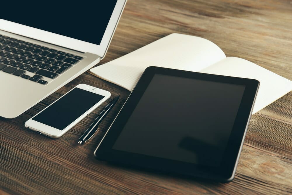 Desk with laptop, cell phone, tablet and notepad and pen