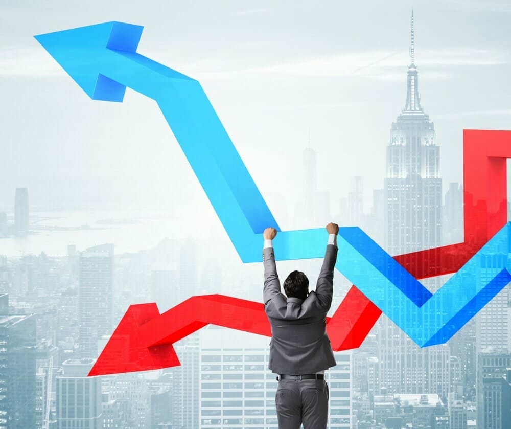A man hanging onto the a blue up-trend arrow with a red down-trend arrow behind and the New York skyline