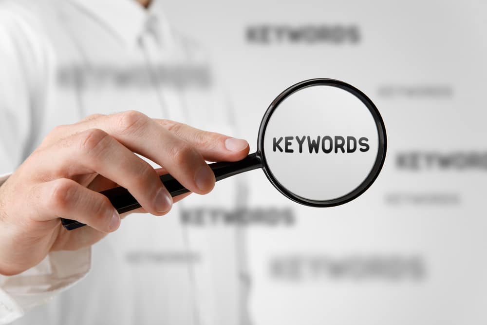 Person holding a magnifying glass over the word "keywords"
