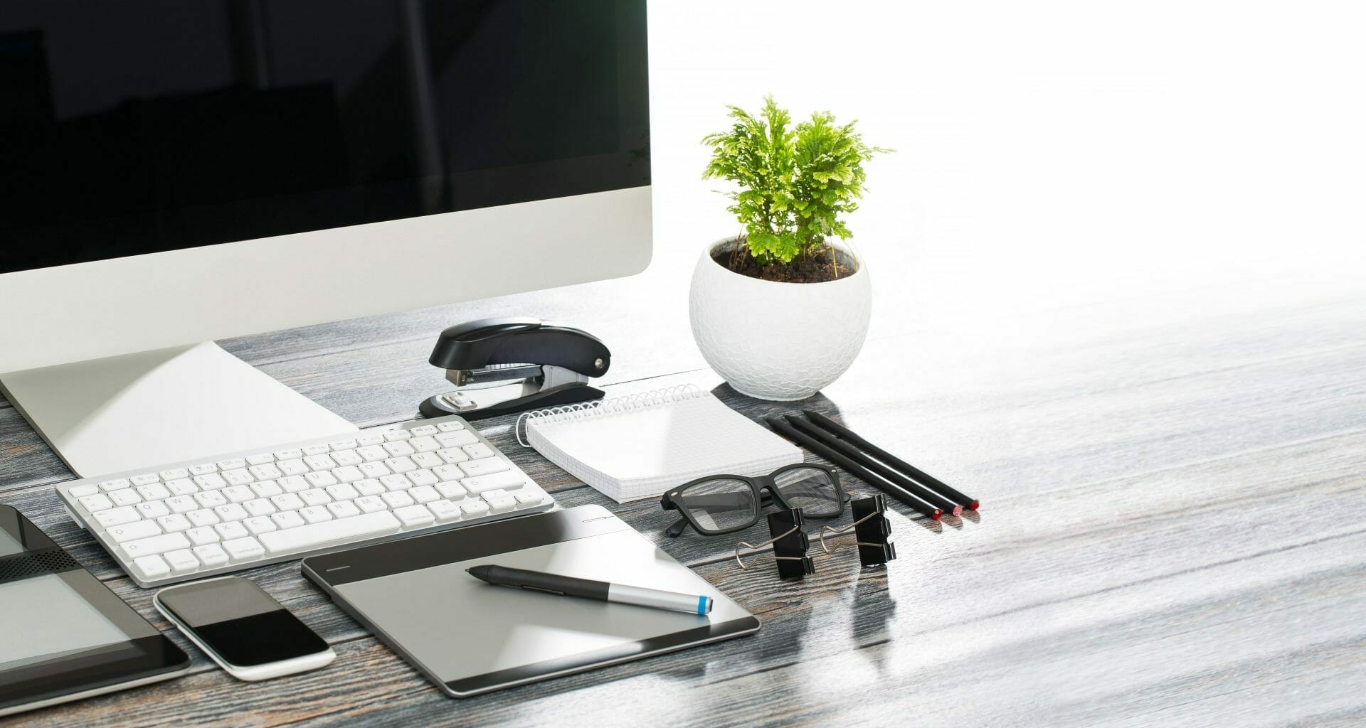 Tidy desk with computer, tablet, cell phone, glasses, pen, pencils, and notepad