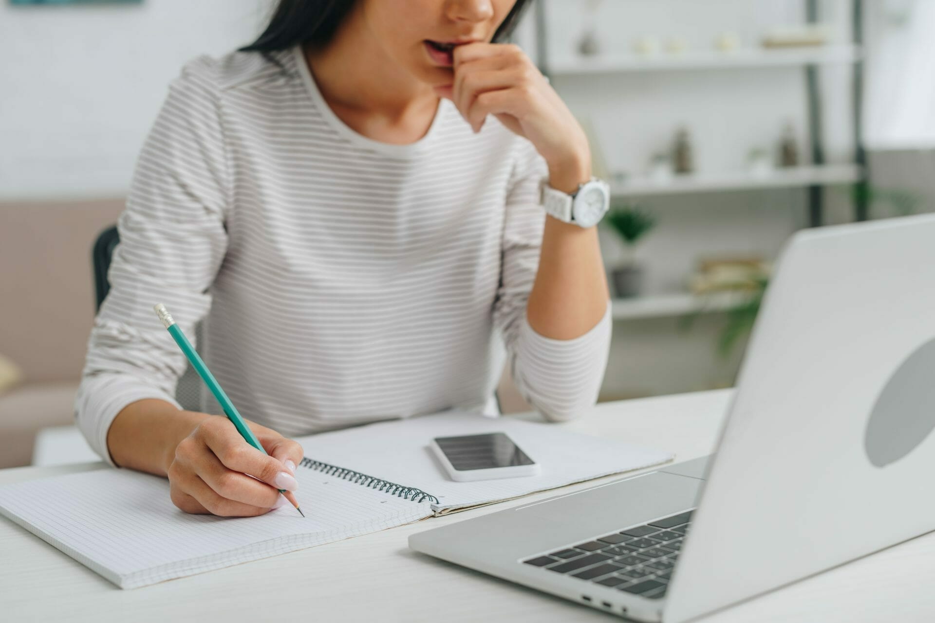 Woman with pad and pencil focused on laptop screen.