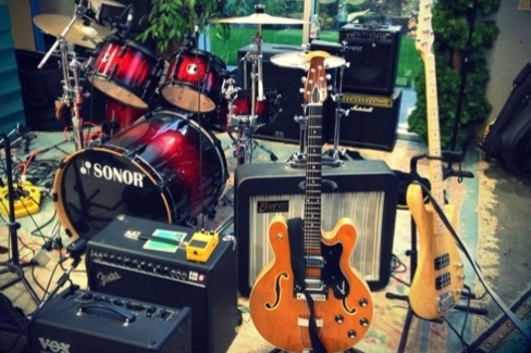 Musical stage setup with guitars, amps, drums, etc.