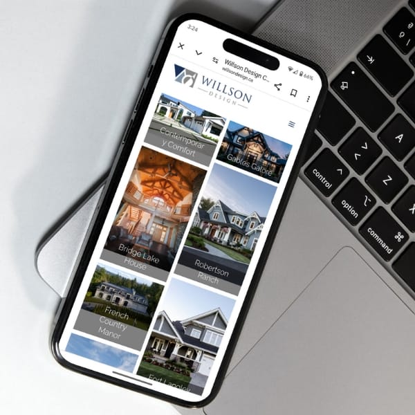 Smartphone displaying a website on a laptop keyboard. The screen shows a real estate site with images of houses labeled "Contemporary Comfort," "Gables Galore," "Bridge Lake House," "Robertson Ranch," and "French Country Manor.